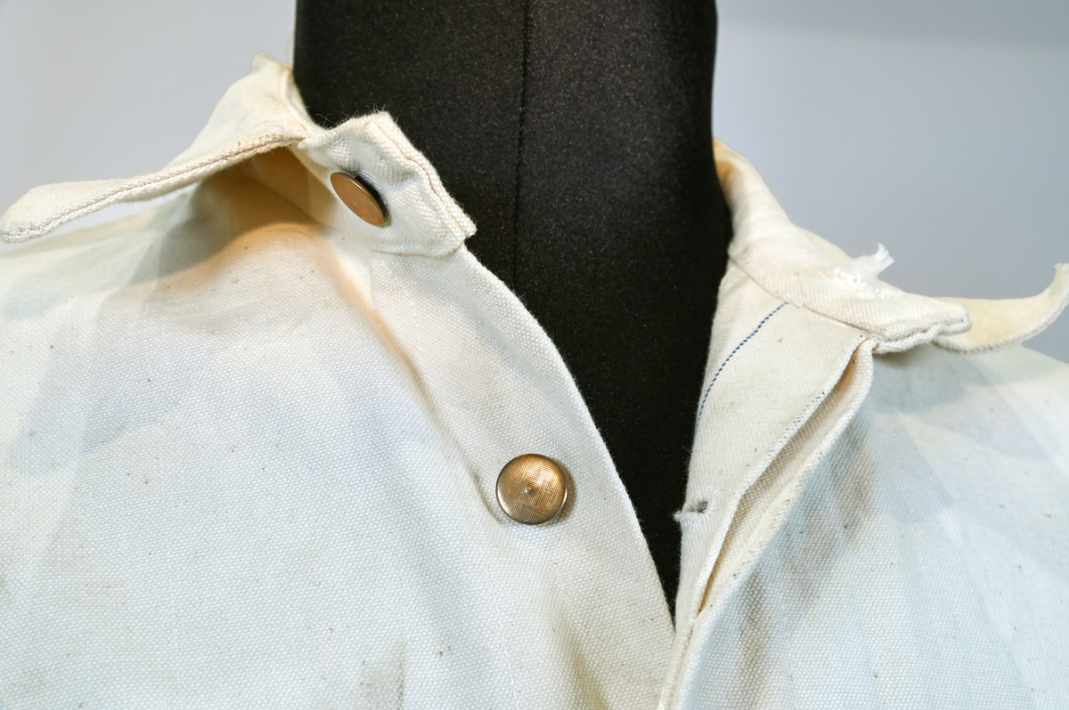 Arbetsoverall i vitt, grövre tyg för personal vid AB Aerotransport. På ryggen finns ett tryck i mörkgrå färg föreställande företagets logga och initialer, ABA. Overallen har två bröstfickor på vardera sida samt två fram- och bakfickor. Under bakfickan på höger ben sitter ytterligare en mindre ficka. Overallen har krage och mässingsfärgade metallknappar. Plagget är utsatt för visst slitage och smuts.