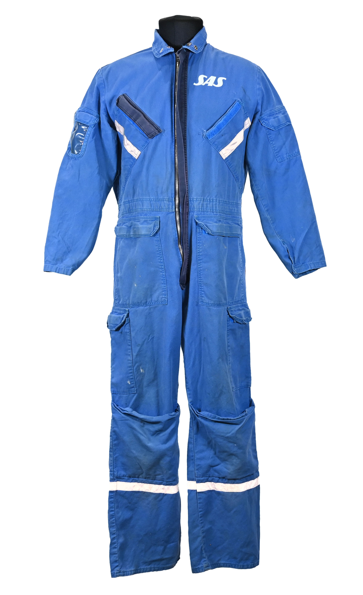Blå arbetsoverall från SAS. På plagget finns en logga för SAS över vänster bröst och mitt på ryggen. Overallen har två bröstfickor med reflexband som försluts med kardborre. Vänster ficka saknar den del som kopplar an till kardborren på fickan. Frampå sitter två större framfickor med lock och på vardera ben sitter ytterligare två fickor på sidorna. På baksidan finns två stora bakfickor. Högt upp på sidan av vardera ärm sitter ytterligare fickor varav den högra är av genomskinlig plast. Samtliga fickor försluts med kardborre. Utöver på bröstfickorna sitter reflexband runt benens nedre del samt högt upp över ryggen. Overallen sluts med dragkedja och två tryckknappar i metall. Ärmsluten kan justeras med kardborre. Vid höfterna finns två öppningar in i overallen. På knäna finns öppningar för att lägga i knäskydd.

På plagget finns spår av vit färg och andra smutsfläckar. Vänster bakficka är nött.

Overallen är producerad av Fristads i storlek 48. På insidan längs med dragskedjan sitter en lapp med texten "OBS! DRAGKEDJAN SKALL VARA STÄNGD VID TVÄTT".