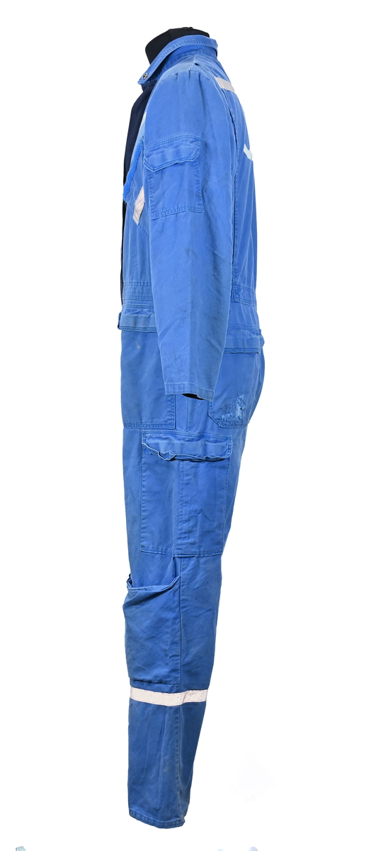 Blå arbetsoverall från SAS. På plagget finns en logga för SAS över vänster bröst och mitt på ryggen. Overallen har två bröstfickor med reflexband som försluts med kardborre. Vänster ficka saknar den del som kopplar an till kardborren på fickan. Frampå sitter två större framfickor med lock och på vardera ben sitter ytterligare två fickor på sidorna. På baksidan finns två stora bakfickor. Högt upp på sidan av vardera ärm sitter ytterligare fickor varav den högra är av genomskinlig plast. Samtliga fickor försluts med kardborre. Utöver på bröstfickorna sitter reflexband runt benens nedre del samt högt upp över ryggen. Overallen sluts med dragkedja och två tryckknappar i metall. Ärmsluten kan justeras med kardborre. Vid höfterna finns två öppningar in i overallen. På knäna finns öppningar för att lägga i knäskydd.

På plagget finns spår av vit färg och andra smutsfläckar. Vänster bakficka är nött.

Overallen är producerad av Fristads i storlek 48. På insidan längs med dragskedjan sitter en lapp med texten "OBS! DRAGKEDJAN SKALL VARA STÄNGD VID TVÄTT".