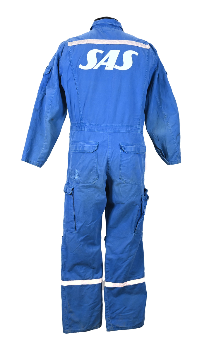 Blå arbetsoverall från SAS. På plagget finns en logga för SAS över vänster bröst och mitt på ryggen. Overallen har två bröstfickor med reflexband som försluts med kardborre. Vänster ficka saknar den del som kopplar an till kardborren på fickan. Frampå sitter två större framfickor med lock och på vardera ben sitter ytterligare två fickor på sidorna. På baksidan finns två stora bakfickor. Högt upp på sidan av vardera ärm sitter ytterligare fickor varav den högra är av genomskinlig plast. Samtliga fickor försluts med kardborre. Utöver på bröstfickorna sitter reflexband runt benens nedre del samt högt upp över ryggen. Overallen sluts med dragkedja och två tryckknappar i metall. Ärmsluten kan justeras med kardborre. Vid höfterna finns två öppningar in i overallen. På knäna finns öppningar för att lägga i knäskydd.

På plagget finns spår av vit färg och andra smutsfläckar. Vänster bakficka är nött.

Overallen är producerad av Fristads i storlek 48. På insidan längs med dragskedjan sitter en lapp med texten "OBS! DRAGKEDJAN SKALL VARA STÄNGD VID TVÄTT".