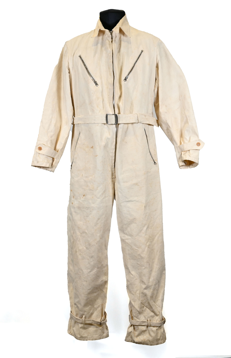 Långärmad overall i vitt tyg med krage. Overallen har två bröstfickor och två framfickor som sluts med dragkedja i metall. I midjan sitter ett bälte i samma material som plagget med ett spänne i metall. Bältet sitter på plats med med två öglor i plaggets sidor. Ärmsluten kan knäppas med tygband och knappar i plast. Bensluten kan spännas med tygband fäst i fyra öglor med metallspänne. 

Overallen är täckt av smuts och fläckar.
