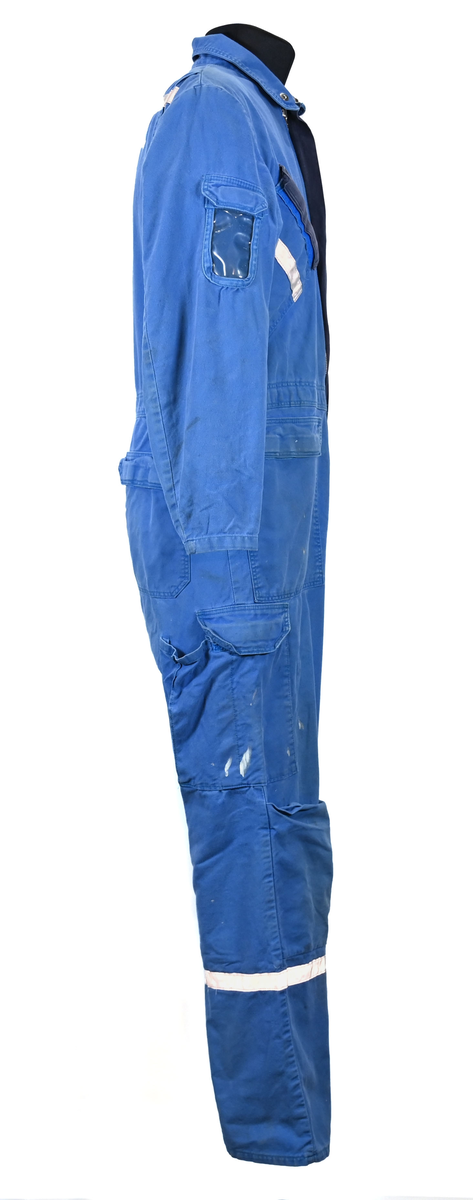 Blå arbetsoverall från SAS. På plagget finns en logga för SAS över vänster bröst och mitt på ryggen. Overallen har två bröstfickor med reflexband som försluts med kardborre. Vänster ficka saknar den del som kopplar an till kardborren på fickan. Frampå sitter två större framfickor med lock och på vardera ben sitter ytterligare två fickor på sidorna. På baksidan finns två stora bakfickor. Högt upp på sidan av vardera ärm sitter ytterligare fickor varav den högra är av genomskinlig plast. Samtliga fickor försluts med kardborre. Utöver på bröstfickorna sitter reflexband runt benens nedre del samt högt upp över ryggen. Overallen sluts med dragkedja och två tryckknappar i metall. Ärmsluten kan justeras med kardborre. Vid höfterna finns två öppningar in i overallen. På knäna finns öppningar för att lägga i knäskydd.

På plagget finns spår av vit färg och andra smutsfläckar. Vänster bakficka är nött.

Overallen är producerad av Fristads i storlek 48. På insidan längs med dragskedjan sitter en lapp med texten "OBS! DRAGKEDJAN SKALL VARA STÄNGD VID TVÄTT".