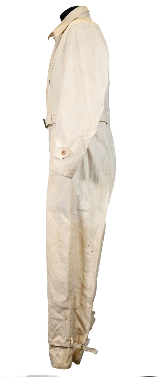 Långärmad overall i vitt tyg med krage. Overallen har två bröstfickor och två framfickor som sluts med dragkedja i metall. I midjan sitter ett bälte i samma material som plagget med ett spänne i metall. Bältet sitter på plats med med två öglor i plaggets sidor. Ärmsluten kan knäppas med tygband och knappar i plast. Bensluten kan spännas med tygband fäst i fyra öglor med metallspänne. 

Overallen är täckt av smuts och fläckar.
