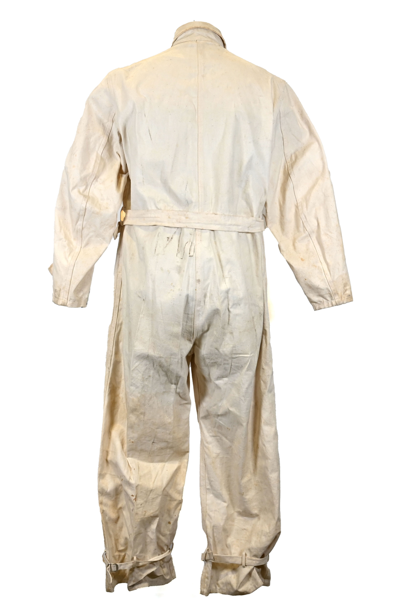 Långärmad overall i vitt tyg med krage. Overallen har två bröstfickor och två framfickor som sluts med dragkedja i metall. I midjan sitter ett bälte i samma material som plagget med ett spänne i metall. Bältet sitter på plats med med två öglor i plaggets sidor. Ärmsluten kan knäppas med tygband och knappar i plast. Bensluten kan spännas med tygband fäst i fyra öglor med metallspänne. 

Overallen är täckt av smuts och fläckar.