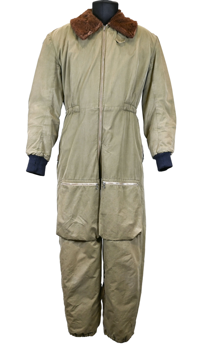 Grågrön overall som använts som flygardräkt. Liknande dräkter har använts inom flygvapnet. Dräkten är fodrad och har en fodrad krage i brun päls. I ärmsluten sitter en mörkblå resår. På framsida lår sitter en ficka på vardera ben som försluts med dragkedja i metall. På sidorna i midjan sitter en öppning som sluts med dragkedja. Dräkten stängs med en lång dragkedja i metall som sträcker sig ned i höger ben. I kragen sitter ett tygband som stänger igen kragen med en plastknapp.  Vid fotändarna finns dragkedja och knapp för att öppna upp fotsluten. 

I tygbandet på kragen satt (borttagen och lagd i ficka av vårdskäl) en lapp fasthäftad som troligtvis har fästs i plagget i samband med tvätt.