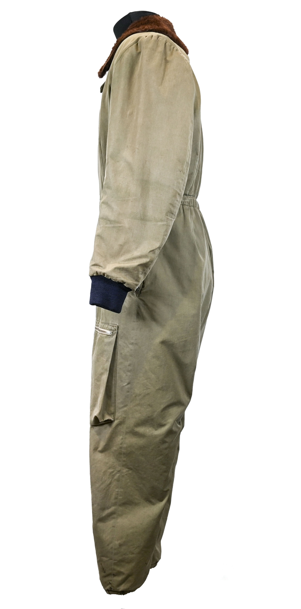 Grågrön overall som använts som flygardräkt. Liknande dräkter har använts inom flygvapnet. Dräkten är fodrad och har en fodrad krage i brun päls. I ärmsluten sitter en mörkblå resår. På framsida lår sitter en ficka på vardera ben som försluts med dragkedja i metall. På sidorna i midjan sitter en öppning som sluts med dragkedja. Dräkten stängs med en lång dragkedja i metall som sträcker sig ned i höger ben. I kragen sitter ett tygband som stänger igen kragen med en plastknapp.  Vid fotändarna finns dragkedja och knapp för att öppna upp fotsluten. 

I tygbandet på kragen satt (borttagen och lagd i ficka av vårdskäl) en lapp fasthäftad som troligtvis har fästs i plagget i samband med tvätt.