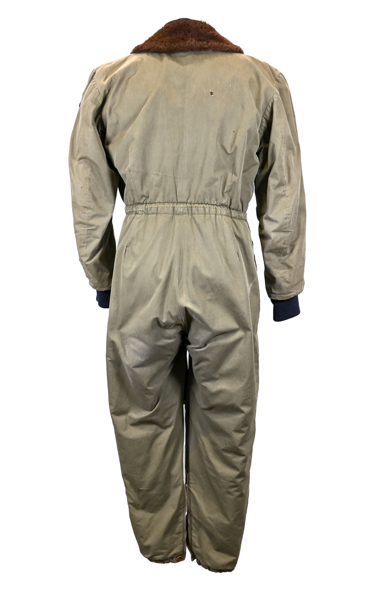 Grågrön overall som använts som flygardräkt. Liknande dräkter har använts inom flygvapnet. Dräkten är fodrad och har en fodrad krage i brun päls. I ärmsluten sitter en mörkblå resår. På framsida lår sitter en ficka på vardera ben som försluts med dragkedja i metall. På sidorna i midjan sitter en öppning som sluts med dragkedja. Dräkten stängs med en lång dragkedja i metall som sträcker sig ned i höger ben. I kragen sitter ett tygband som stänger igen kragen med en plastknapp.  Vid fotändarna finns dragkedja och knapp för att öppna upp fotsluten. 

I tygbandet på kragen satt (borttagen och lagd i ficka av vårdskäl) en lapp fasthäftad som troligtvis har fästs i plagget i samband med tvätt.