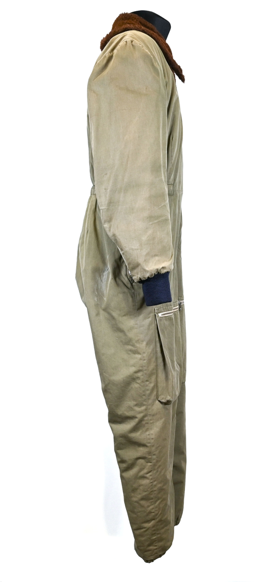 Grågrön overall som använts som flygardräkt. Liknande dräkter har använts inom flygvapnet. Dräkten är fodrad och har en fodrad krage i brun päls. I ärmsluten sitter en mörkblå resår. På framsida lår sitter en ficka på vardera ben som försluts med dragkedja i metall. På sidorna i midjan sitter en öppning som sluts med dragkedja. Dräkten stängs med en lång dragkedja i metall som sträcker sig ned i höger ben. I kragen sitter ett tygband som stänger igen kragen med en plastknapp.  Vid fotändarna finns dragkedja och knapp för att öppna upp fotsluten. 

I tygbandet på kragen satt (borttagen och lagd i ficka av vårdskäl) en lapp fasthäftad som troligtvis har fästs i plagget i samband med tvätt.