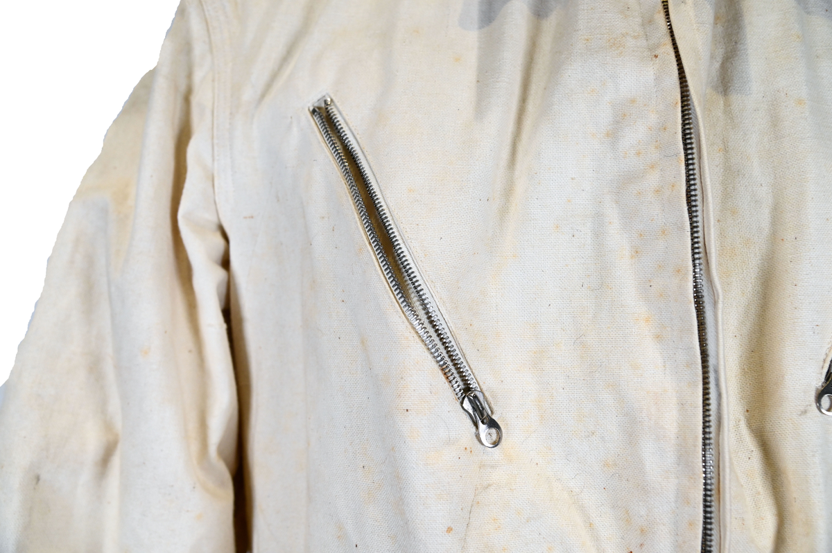 Långärmad overall i vitt tyg med krage. Overallen har två bröstfickor och två framfickor som sluts med dragkedja i metall. I midjan sitter ett bälte i samma material som plagget med ett spänne i metall. Bältet sitter på plats med med två öglor i plaggets sidor. Ärmsluten kan knäppas med tygband och knappar i plast. Bensluten kan spännas med tygband fäst i fyra öglor med metallspänne. 

Overallen är täckt av smuts och fläckar.