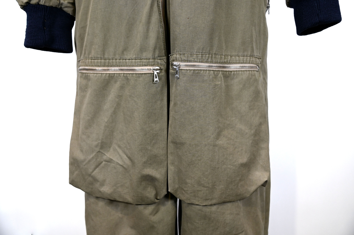 Grågrön overall som använts som flygardräkt. Liknande dräkter har använts inom flygvapnet. Dräkten är fodrad och har en fodrad krage i brun päls. I ärmsluten sitter en mörkblå resår. På framsida lår sitter en ficka på vardera ben som försluts med dragkedja i metall. På sidorna i midjan sitter en öppning som sluts med dragkedja. Dräkten stängs med en lång dragkedja i metall som sträcker sig ned i höger ben. I kragen sitter ett tygband som stänger igen kragen med en plastknapp.  Vid fotändarna finns dragkedja och knapp för att öppna upp fotsluten. 

I tygbandet på kragen satt (borttagen och lagd i ficka av vårdskäl) en lapp fasthäftad som troligtvis har fästs i plagget i samband med tvätt.