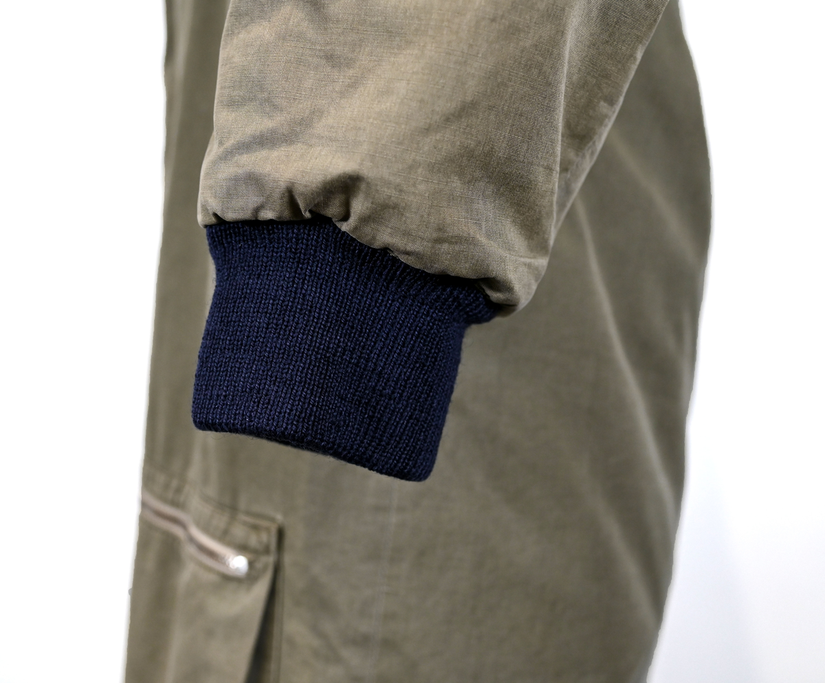 Grågrön overall som använts som flygardräkt. Liknande dräkter har använts inom flygvapnet. Dräkten är fodrad och har en fodrad krage i brun päls. I ärmsluten sitter en mörkblå resår. På framsida lår sitter en ficka på vardera ben som försluts med dragkedja i metall. På sidorna i midjan sitter en öppning som sluts med dragkedja. Dräkten stängs med en lång dragkedja i metall som sträcker sig ned i höger ben. I kragen sitter ett tygband som stänger igen kragen med en plastknapp.  Vid fotändarna finns dragkedja och knapp för att öppna upp fotsluten. 

I tygbandet på kragen satt (borttagen och lagd i ficka av vårdskäl) en lapp fasthäftad som troligtvis har fästs i plagget i samband med tvätt.