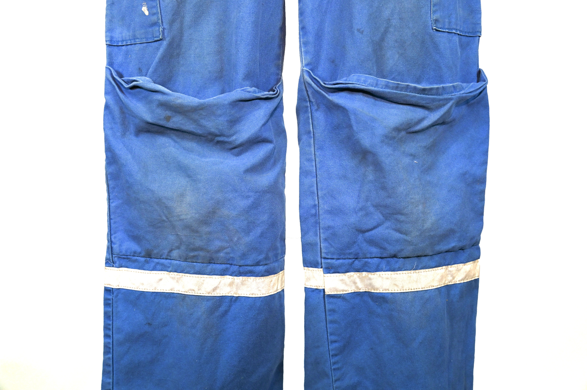 Blå arbetsoverall från SAS. På plagget finns en logga för SAS över vänster bröst och mitt på ryggen. Overallen har två bröstfickor med reflexband som försluts med kardborre. Vänster ficka saknar den del som kopplar an till kardborren på fickan. Frampå sitter två större framfickor med lock och på vardera ben sitter ytterligare två fickor på sidorna. På baksidan finns två stora bakfickor. Högt upp på sidan av vardera ärm sitter ytterligare fickor varav den högra är av genomskinlig plast. Samtliga fickor försluts med kardborre. Utöver på bröstfickorna sitter reflexband runt benens nedre del samt högt upp över ryggen. Overallen sluts med dragkedja och två tryckknappar i metall. Ärmsluten kan justeras med kardborre. Vid höfterna finns två öppningar in i overallen. På knäna finns öppningar för att lägga i knäskydd.

På plagget finns spår av vit färg och andra smutsfläckar. Vänster bakficka är nött.

Overallen är producerad av Fristads i storlek 48. På insidan längs med dragskedjan sitter en lapp med texten "OBS! DRAGKEDJAN SKALL VARA STÄNGD VID TVÄTT".