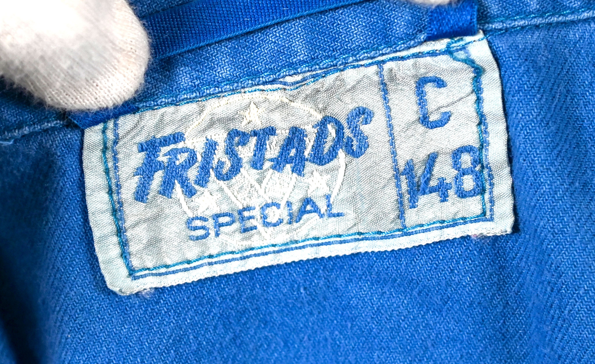 Blå arbetsoverall från SAS. På plagget finns en logga för SAS över vänster bröst och mitt på ryggen. Overallen har två bröstfickor med reflexband som försluts med kardborre. Vänster ficka saknar den del som kopplar an till kardborren på fickan. Frampå sitter två större framfickor med lock och på vardera ben sitter ytterligare två fickor på sidorna. På baksidan finns två stora bakfickor. Högt upp på sidan av vardera ärm sitter ytterligare fickor varav den högra är av genomskinlig plast. Samtliga fickor försluts med kardborre. Utöver på bröstfickorna sitter reflexband runt benens nedre del samt högt upp över ryggen. Overallen sluts med dragkedja och två tryckknappar i metall. Ärmsluten kan justeras med kardborre. Vid höfterna finns två öppningar in i overallen. På knäna finns öppningar för att lägga i knäskydd.

På plagget finns spår av vit färg och andra smutsfläckar. Vänster bakficka är nött.

Overallen är producerad av Fristads i storlek 48. På insidan längs med dragskedjan sitter en lapp med texten "OBS! DRAGKEDJAN SKALL VARA STÄNGD VID TVÄTT".