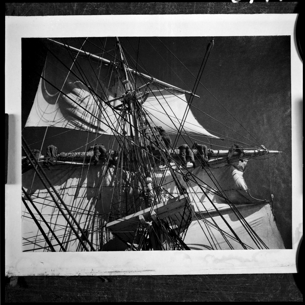 Bilden visar verksamhet ombord på skeppsgossefartyget Jarramas. Manskapet har klättrat upp på riggen och håller på att sätta eller bärga segel.
Fotot är taget under något av åren 1940-talet, då fartyget var bemannat av elever från Sjömannsskolan.