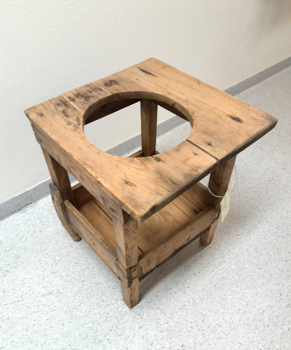 Ståstol (gåstol) for barn. Trekvit. Rundt hol i overplata. Fire rette firkanta bein. Underplate for føtene. 