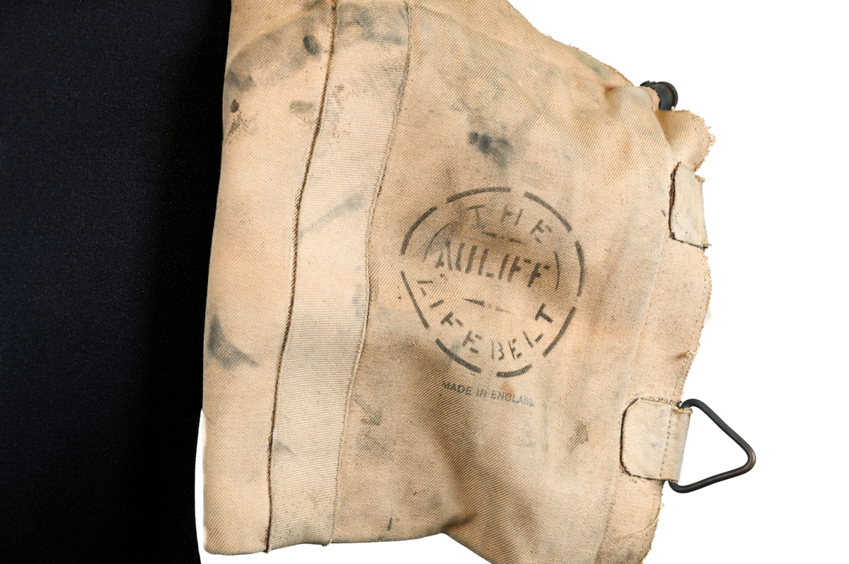 Flytväst, "The Auliff Lifebelt", uppblåsbar, tillverkad av duk och gummi, med metallfäste fram och axelband av tyg. Ursprunlingen var föremålet utrustad med en gasbehållare och ett metallhandtag som aktiverade uppblåsningsmekanismen. Flytvästen användes ovanpå flygardräkten och har därför en stor omkrets.