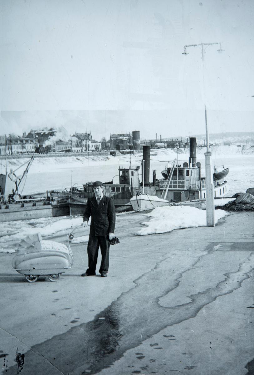 Jens Mikkelsen ( 18.11.1929 - 22.12.2015 ) med Anne Grethe Mikkelsen i vognen ( 09.09.1953 ). Far og datter på søndagstur til Hamar brygge vinteren 1954. Damskipet Dølen skimtes i bakgrunn.