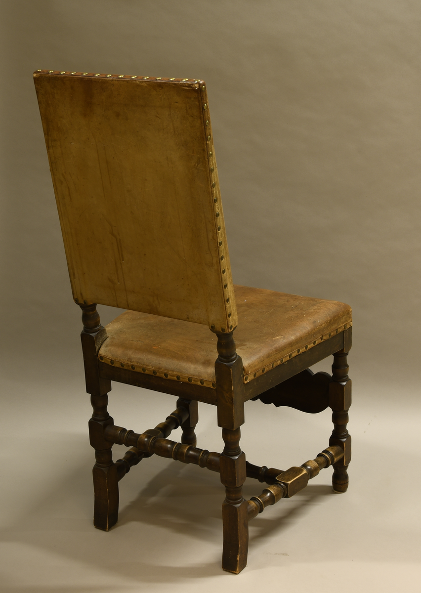 Stol av tre, med trekk av skinn. Stolen har dreide bein med rund og firkantet profil. Nederst er det en H-formet sprosse av dreid treverk, og det er en dreid sprosse mellom bakbeina. På framsiden er det en sprosse med akantusblad og i midten tre palmetter med gjennombrutte mellompartier. Ryggen har stående rektangulær form og er trukket med skinn på fram- og bakside. Setet er også trukket med skinn. Skinnet er festet med messingnagler.