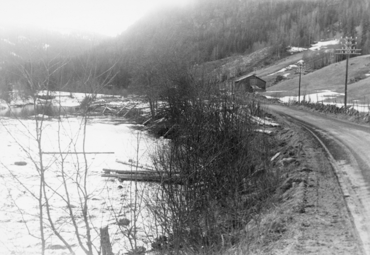 Tømmertillegging i Gausdal våren 1961. Fløtingsfunksjonæren som tok bildet har notert seg navnet Hole. Motivet kan være fra Svatsum i Vestre Gausdal. Elva er i så fall Jøra. Fotografen har stått ved kanten av en veg som her gikk helt inntil vassdraget, med en del krattskog i elveskråningen. Bak den bladløse vegetasjonen skimter vi ei lita slette som må ha fungert som velteplass. Tømmeret der ser ut til å ha vært noe uryddig tillagt, og fotografen har notert seg at noe av det lå for langt ut. På den andre sida av det som antas å ha vært Vestringsvegen var det oppsatt en skigard mot et engareal, og nederst på denne innmarka sto det ei laftet høyløe. I den bratte lia i bakgrunnen vokste skogen tett.