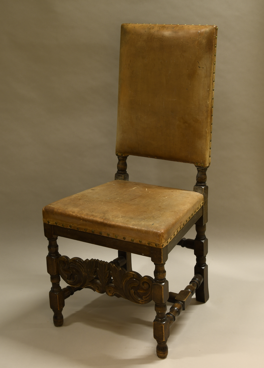 Stol av tre, med trekk av skinn. Stolen har dreide bein med rund og firkantet profil. Nederst er det en H-formet sprosse av dreid treverk, og det er en dreid sprosse mellom bakbeina. På framsiden er det en sprosse med akantusblad og i midten tre palmetter med gjennombrutte mellompartier. Ryggen har stående rektangulær form og er trukket med skinn på fram- og bakside. Setet er også trukket med skinn. Skinnet er festet med messingnagler.
