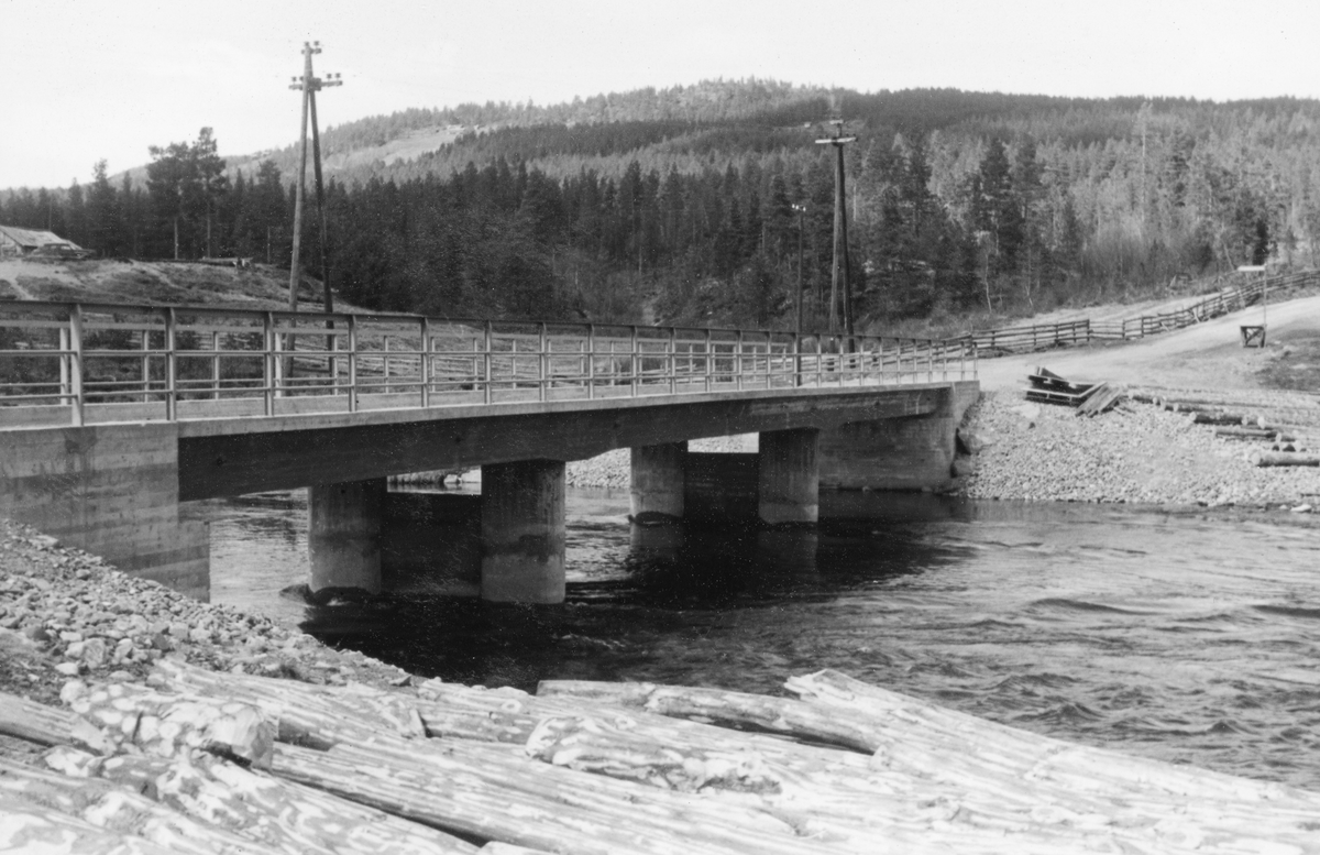Slangen bru i Skåbu i Nord-Fron. Dette fotografiet ble tatt i mai 1961, på et tidspunkt da denne brua må ha vært ny. Det dreier seg om ei bjelkebru av betong med stålrekkverk på begge sider. Brua bæres av støpte landkar i elveskråningene og av to søylepar som deler elva i tre løp. Brua krysser Slangslona, den korte elvestrekningen mellom innsjøene Slangen og Olstappen som ligger henholdsvis 668 og 667 meter over havet. Vegen over brua heter Slangslivegen.
