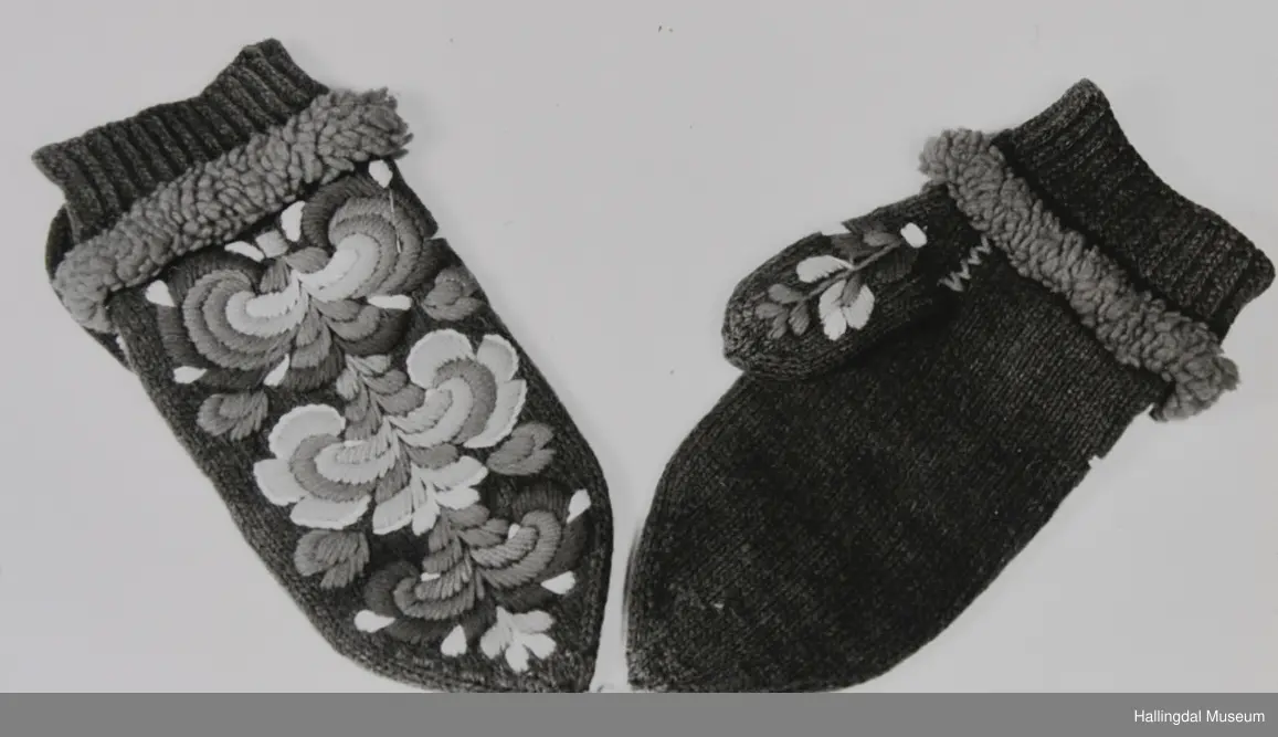 Votter i glattstrikking. Ullbroderi, stilisert rosemotiv i fargane kvitt, gult, oransje, rosa, raudt, fiolett og blått. Det er hallingsaum. Mellom broderi og vrangbord ei raud bord med tette trafs (frynser). Lite motiv i kvitt, gult, rosa og raudt på tommelen.