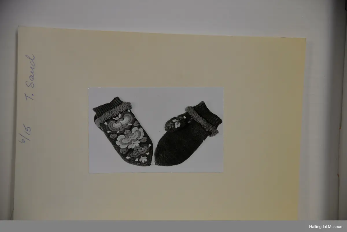 Votter i glattstrikking. Ullbroderi, stilisert rosemotiv i fargane kvitt, gult, oransje, rosa, raudt, fiolett og blått. Det er hallingsaum. Mellom broderi og vrangbord ei raud bord med tette trafs (frynser). Lite motiv i kvitt, gult, rosa og raudt på tommelen.