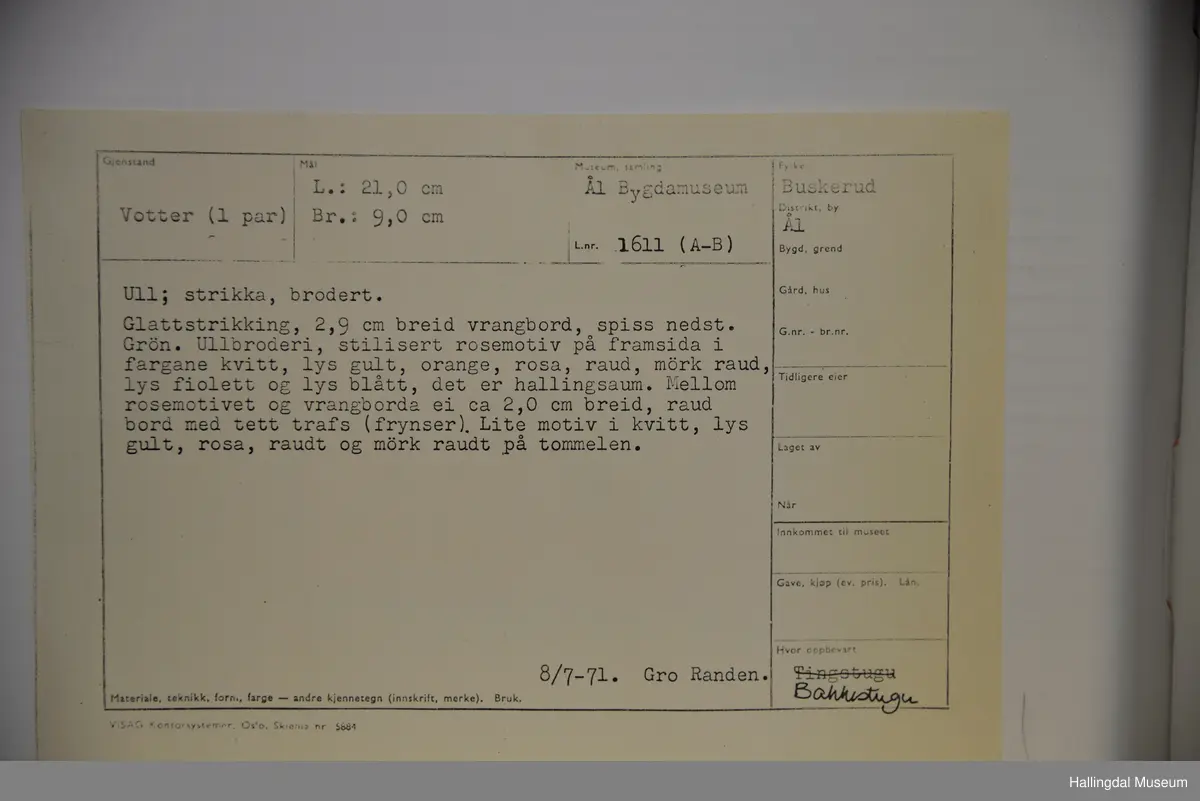 Votter i glattstrikking. Ullbroderi, stilisert rosemotiv i fargane kvitt, gult, oransje, rosa, raudt, fiolett og blått. Det er hallingsaum. Mellom broderi og vrangbord ei raud bord med tette trafs (frynser). Lite motiv i kvitt, gult, rosa og raudt på tommelen.
