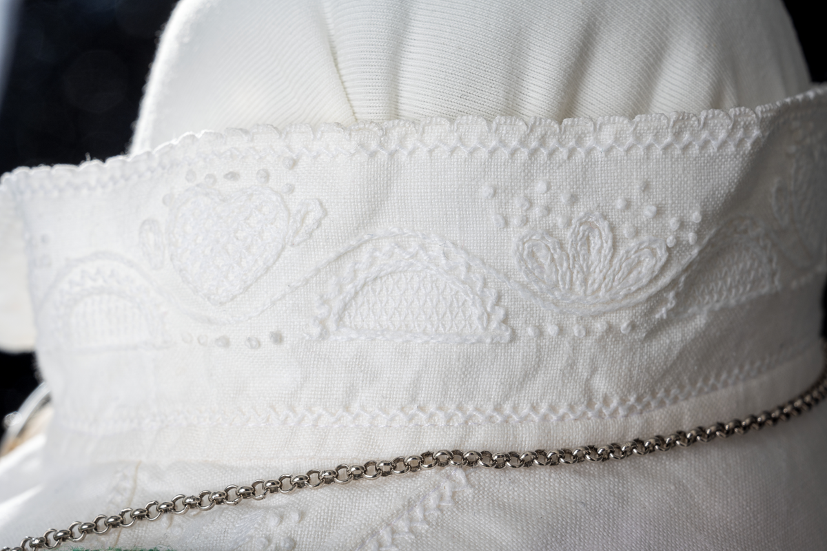Trønderbunad med grønn ullstakk. Grønn vest med mønster "rose med bølge", ulldamask med hvit lin i renning og ull i innslag. Veske i sort ullstoff med flerfarget broderi med mønster "sokndal rust", bakstykke av skinn, foret med baskerlin, forsølvet veskelås. Skjorte av hvit lin, rikt broderte mansjetter, halslinning og skulderstykke, såkalt "festskjorte" med rankesøm og uttrekkssøm på ermene og brystet.