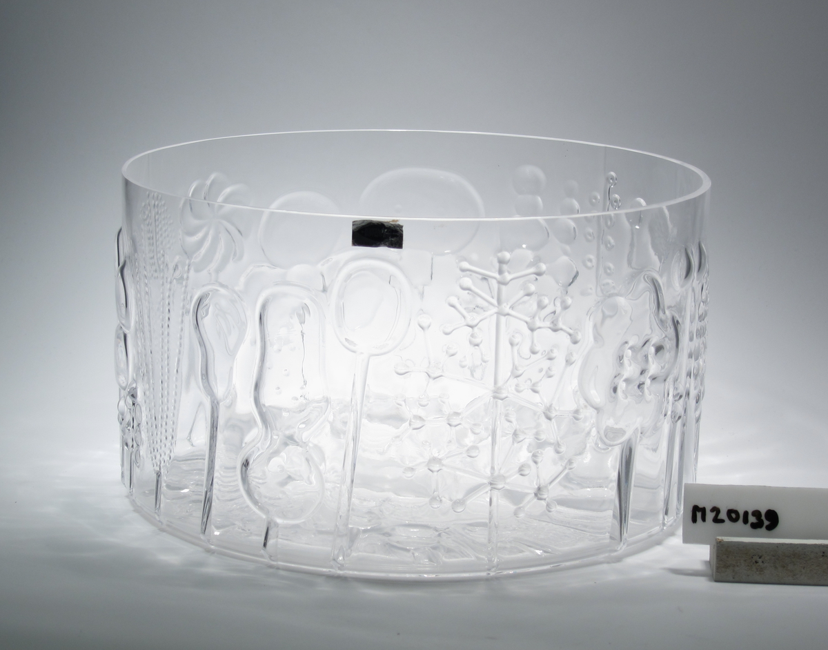 "Flora" Formgivare: Oiva Toikka. Cylinderformad skål med fantasifull blomrelief runt om och i botten.