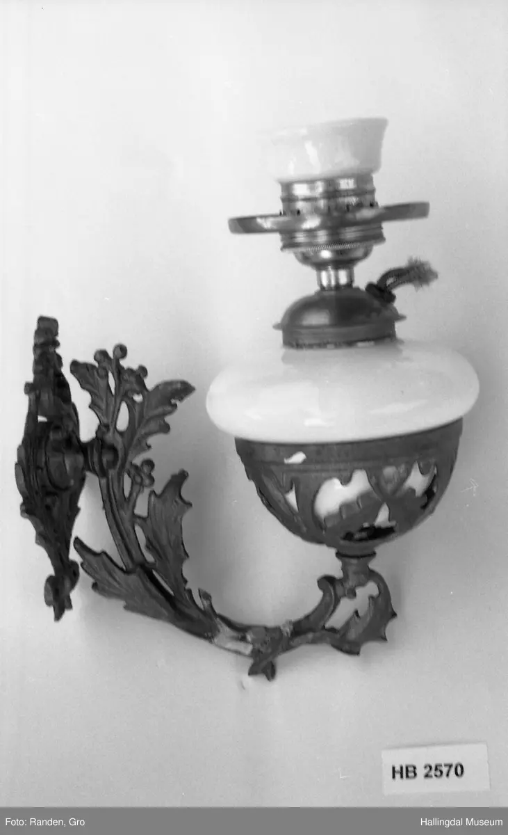 Vegghengt parafinlampe i rokokkostil med kolbe og skjerm.