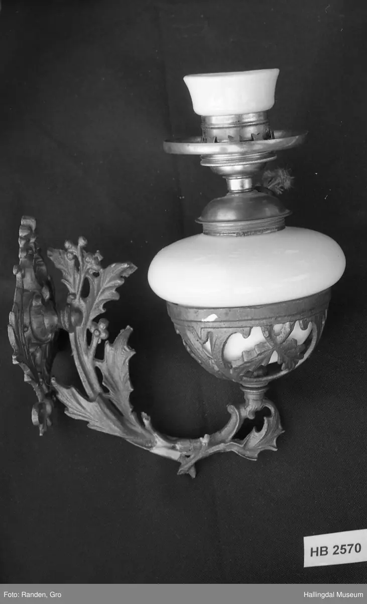 Vegghengt parafinlampe i rokokkostil med kolbe og skjerm.