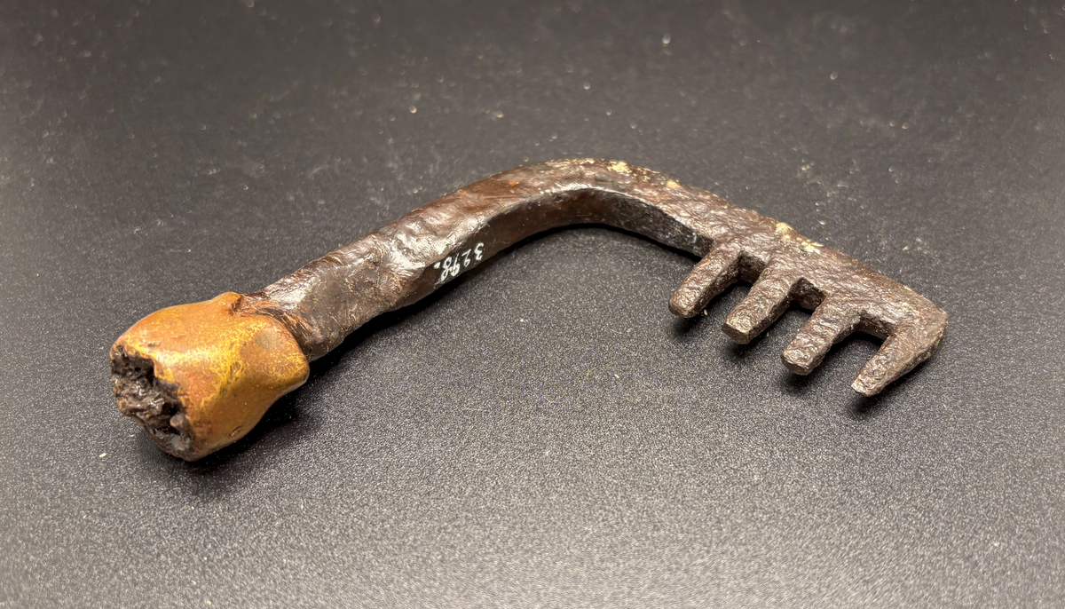 Fyr-kloigt ax vinkelrätt avsatt mot skaftet  detta är en bit upp omlindat med ett 23 mm brett bronsband ovanför det är skaftet avbrutet enligt orginalkatalogen funnet vid odling av äng 1884 i hummelbos
av järn, och med brons, 4 3/8 tum hög, funnen 1884 vid odling i äng, vid hummelbos.