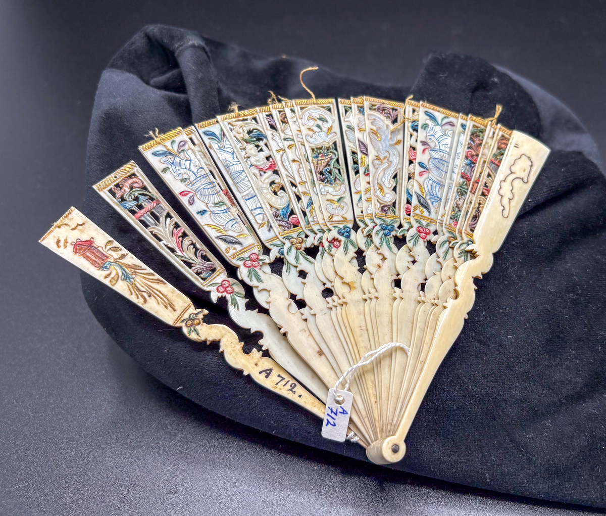 Solfjäder av elfenben med genombrutet mönster, snidad relief, pärlemorinläggningar? och målad (även baksidan). Defekt, endast nedre delen bevarad. Inskrivet 2006-12-05, SH.
Av elfenben, genombrutet mönster, förgylld, defekt, halv