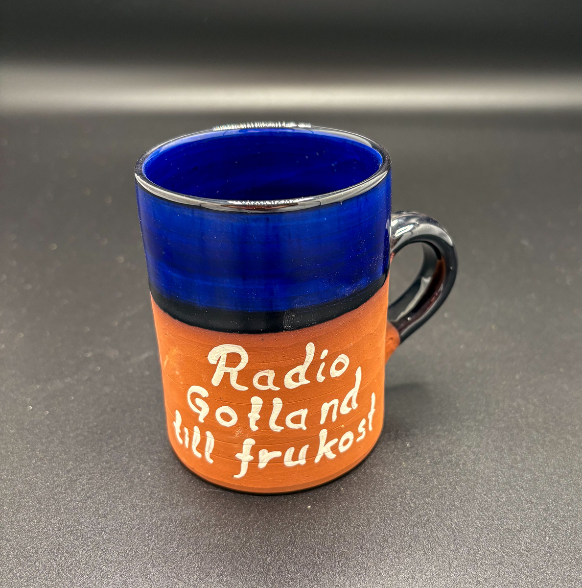Två keramikmuggar tillverkade av gotlandskeramikern Agge Ahlin. Adresslapp finns ännu kvar på den ena koppen: "Tillv. Agge Ahlin, Förs. Strandg. 9, Visby". Godset är även signerat med AA Visby.

Muggarnas övre del samt muggens inre är glaserade i blått, örat är glaserat i svart. Mer än hälften av muggen är oglaserad men har en text skriven i vitt: "Radio Gotland till frukost".