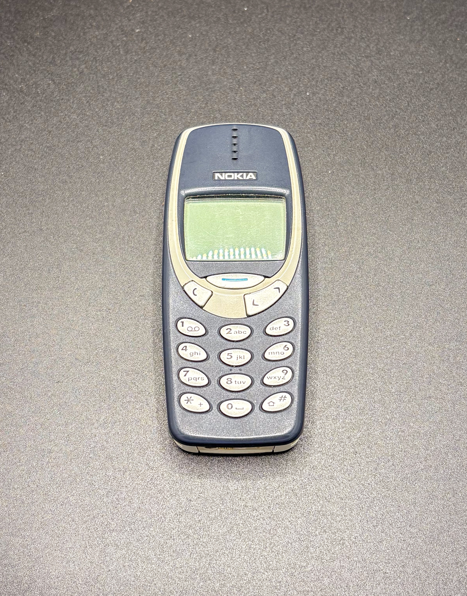Nokia mobiltelefon modell 3310. Skal av mörkblått plast med silverfärgade knappar och rektangulär display. I originalkartong med laddare, billaddare, instruktionsbok och inköpskvitto.