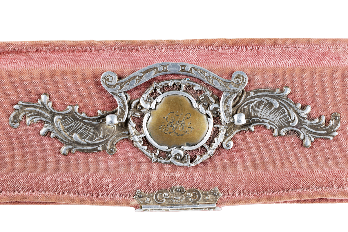 Klätt med ljusrött plysch, fodrat med silkesatin. Grå metallbeslag i nyrokoko och ledat handtag på locket. Beslaget med förgylld kartusch i mitten med ingraverade initialer: "AJC". Beslag i hörnen på etuiets framsida och vid låset. Kulformade metallfötter. 

Till etuiet hör handskar BM 70641.