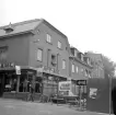 Hörnet Apotekaregatan-Storgatan i Linköping. Sedan bilden togs 1972 är miljön i blickfånget närmast oförändrad. Till höger i bilden anas emellertid en vid tiden pågående och påfallande omgestaltning av stadsbilden. Efterhand skulle bildens husfasader skymmas av handelshuset Filbyters kolossala huskropp.