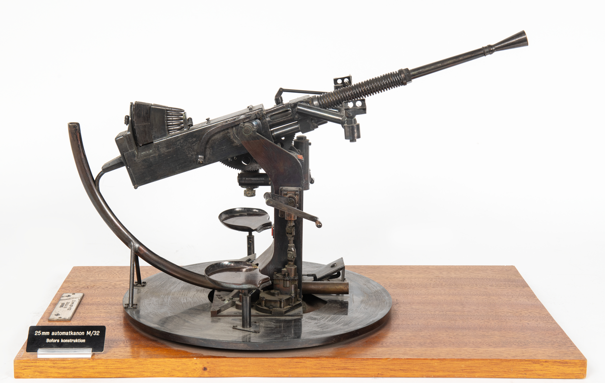 Modell av 25 mm apj M/32 med patronmagasin. 
Modellen är svartbetsad och monterad på en rektangulär skiva av mahogny.