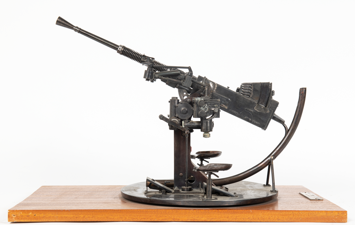 Modell av 25 mm apj M/32 med patronmagasin. 
Modellen är svartbetsad och monterad på en rektangulär skiva av mahogny.