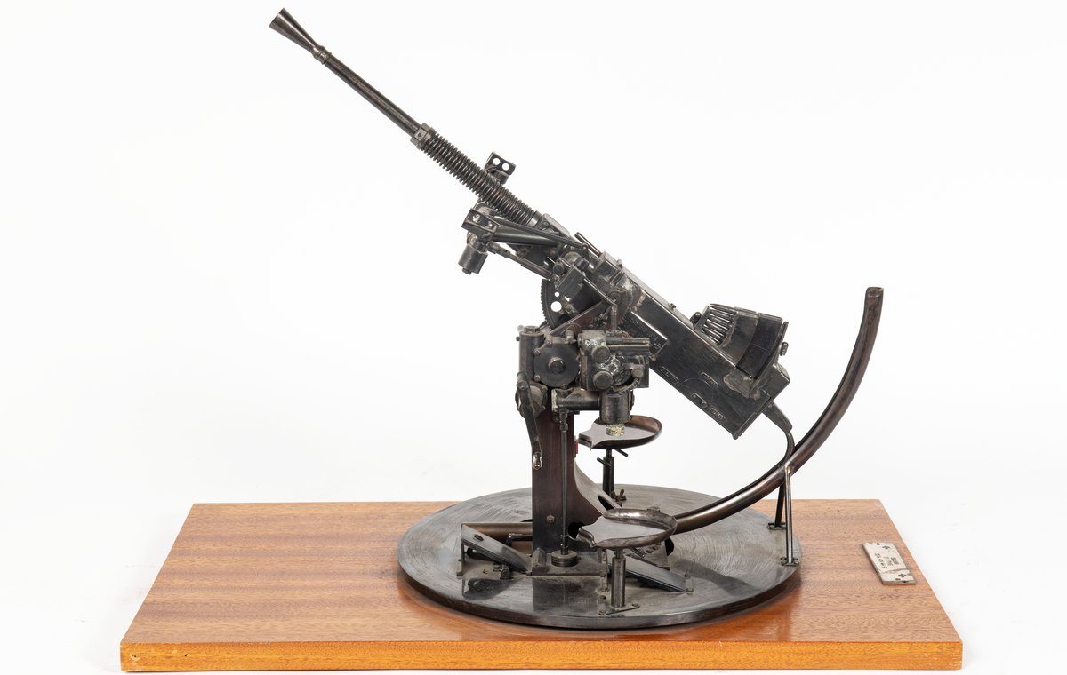 Modell av 25 mm apj M/32 med patronmagasin. 
Modellen är svartbetsad och monterad på en rektangulär skiva av mahogny.