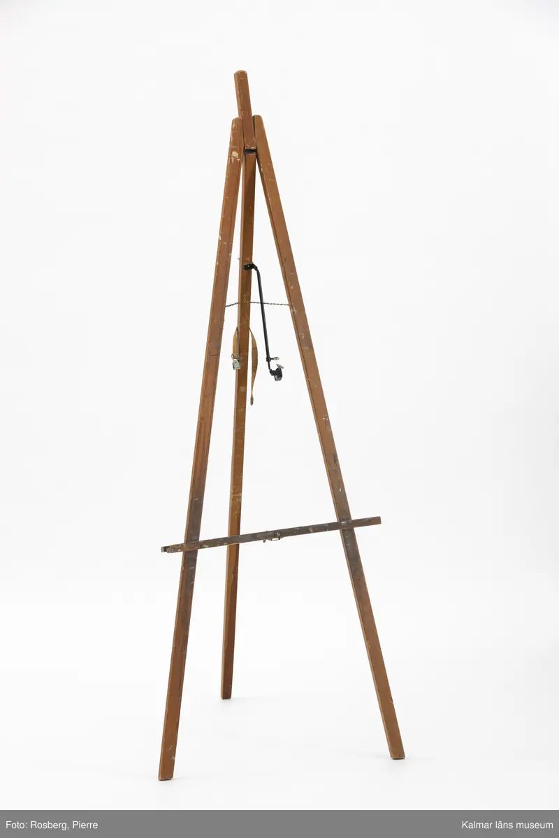 KLM 46734:1. Staffli. Golvstaffli av trä med tre ben, kedja och skruvstöd av metall. Rem av textil  på bakre benet, används i hopfällt läge. På baksidan tillverkarmärke av mässing med text: Beckers MADE IN SWEDEN. I kedjan hänger ett runt företagsmärke av metall och papper med text: A.B. WILH. BECKER KONSTNÄRSMATERIAL. Löst skruvstöd, del till staffli.