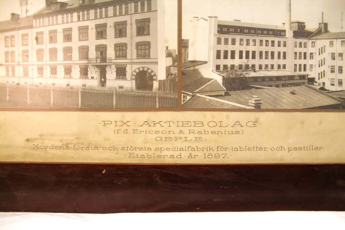 Två inramade fotografier av Reimers från 1919 med text. Bilderna visar Pix AB:s byggnader i Gävle. Texten lyder: "PIX AKTIEBOLAG (tidigare Ericson & Rabenius) GEFLE / Nordens första och största specialfabrik för tabletter och pastiller / Etablerad år 1897". Mörkbetsad träram och glas.