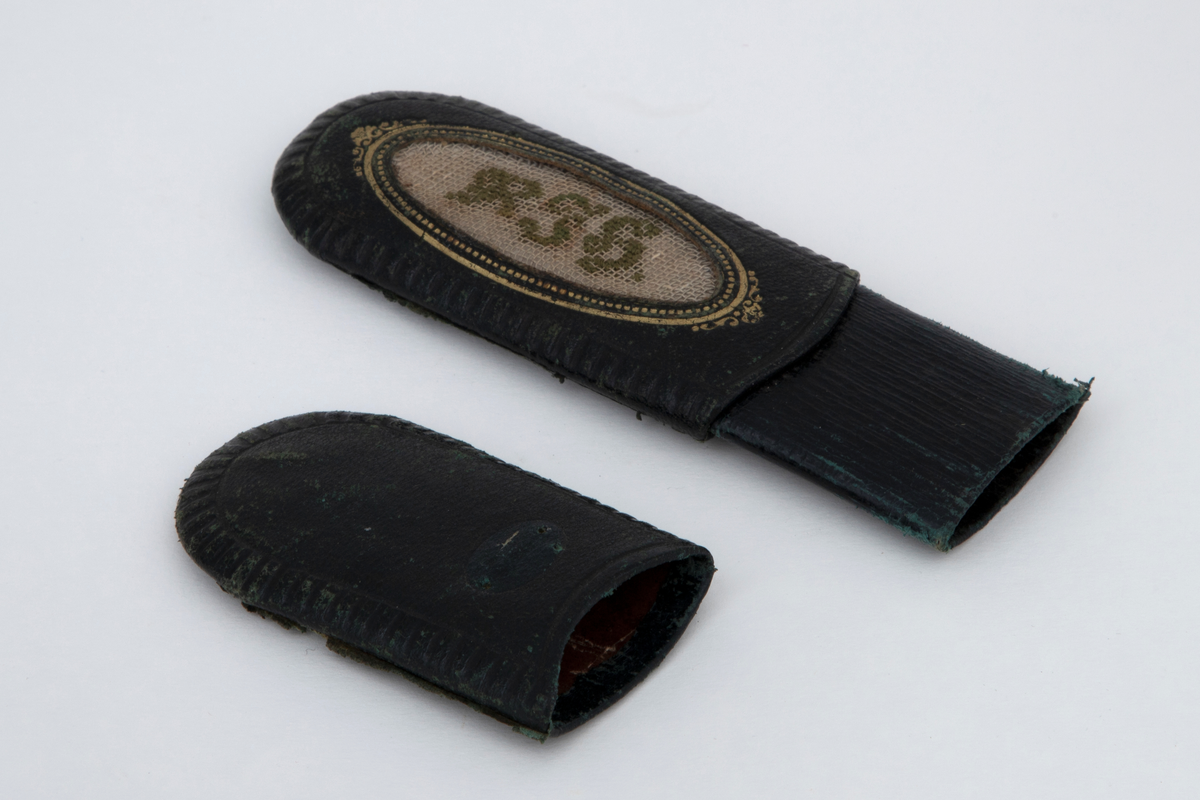 Briller i etui. Små ovale glass, innfattet i en tynn ståltrådsramme med hengslede, trådtynne, bøyde stålstenger med knoppformet avslutning. Todelt etui av papp, trukket med mørkeblått skinn, glatt med riflet kant. På etuiets største del er det et utspart felt omgitt av en ramme i gulltrykk. I feltet er det broderte grønne initialer på hvit stramei: R. J. H.