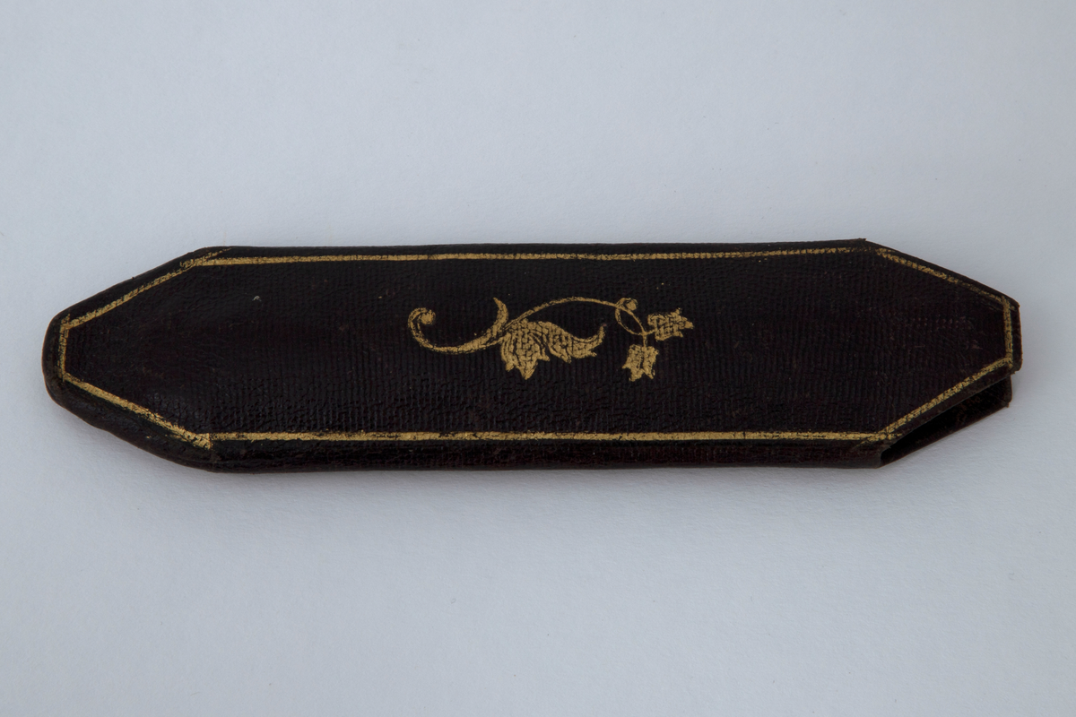 Briller i etui. Små ovale glass i innfatning av tynn stålstreng med hengslede, rette stenger som er svakt bøyd og har hempeform ved avslutningen. Etuiet er smalt med åpning i den ene enden. Trukket med tynt, brunt skinn med innpressede gullornamenter.