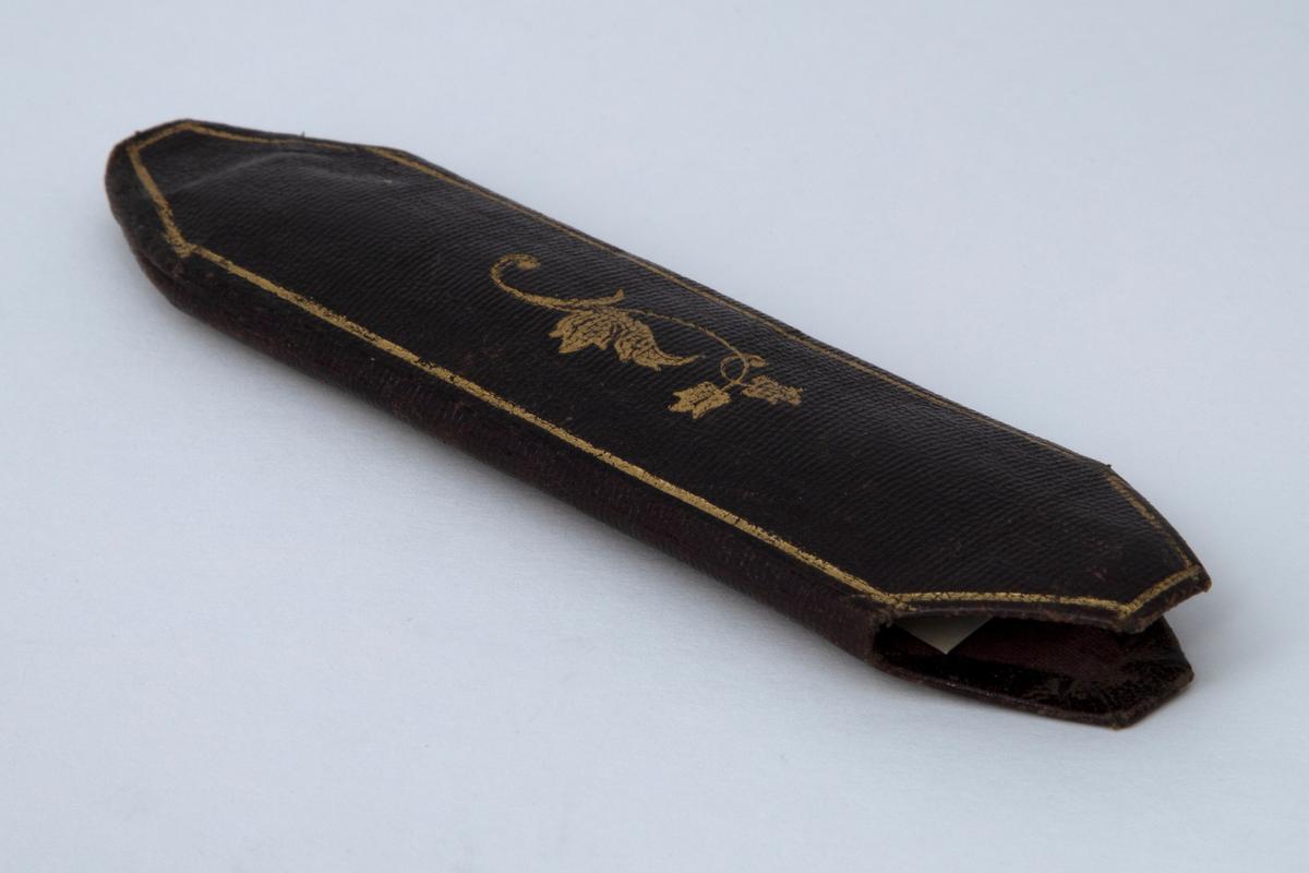 Briller i etui. Små ovale glass i innfatning av tynn stålstreng med hengslede, rette stenger som er svakt bøyd og har hempeform ved avslutningen. Etuiet er smalt med åpning i den ene enden. Trukket med tynt, brunt skinn med innpressede gullornamenter.