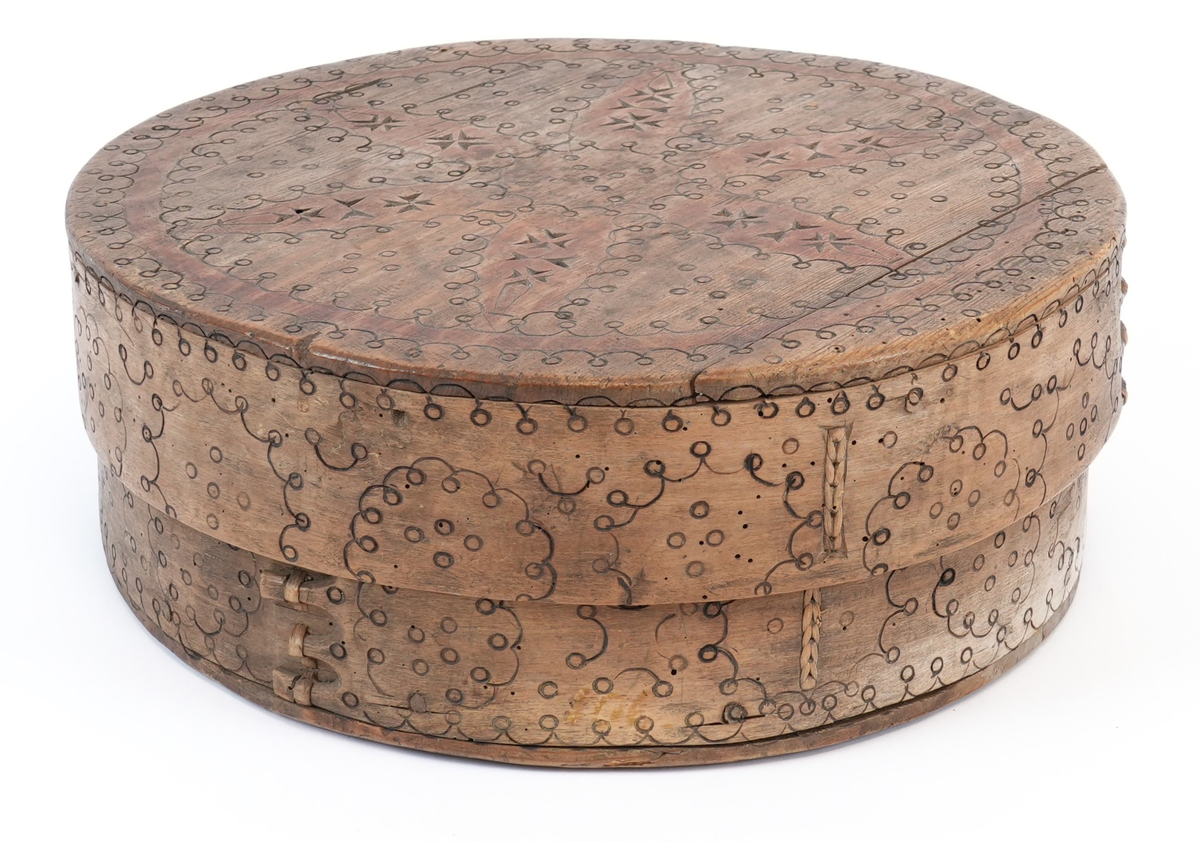 Svidekor over heile øskja. På toppen av lokket ei stor, sentral seksbladrose innskriven i ein sirkel med to melteserkors på kvert roseblad. Rosa og sirkelen måla raud. Langs sida sirklar av bogar og ringar. Alle linjene i ornamentet har form av svidde, små bogar og ringar.