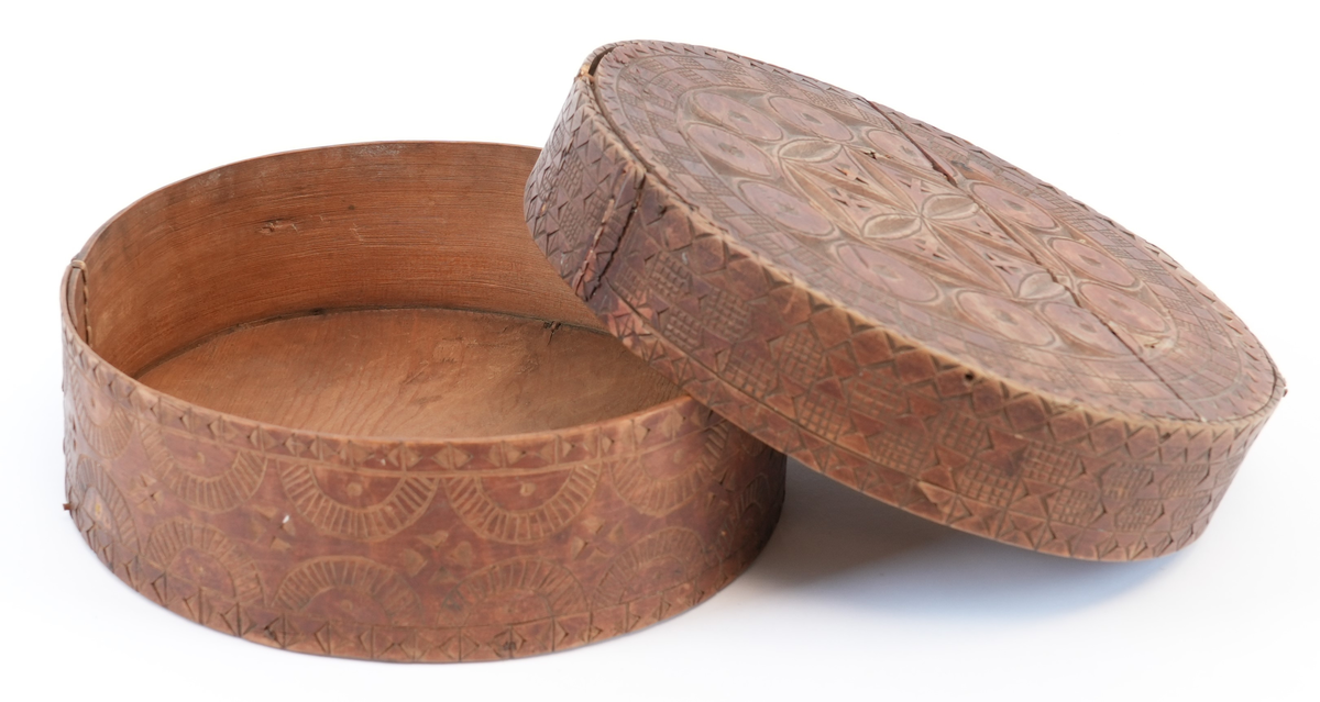 Karveskurd over heile øskja. På toppen av lokket ei sentral seksbladrose innskriven i ein sekskant med konkave sider, alt i ein sirkel. Mellom roseblader utskorne krysskors. Rundt rosa ei brei stripe med utskorne sirklar. Rundt dei, eit maskulint muruspjeld og sikksakk langs kanten. På sideveggen av lokket dobbel sikksakk langs kanten og muruspjeld med vekslende felt (rutenett og ståande timeglass symbol). På sideveggen av behaldaren, langs kantane stripar med ståande timeglass symbol. Mellom dei halvsirklar og krysskors.