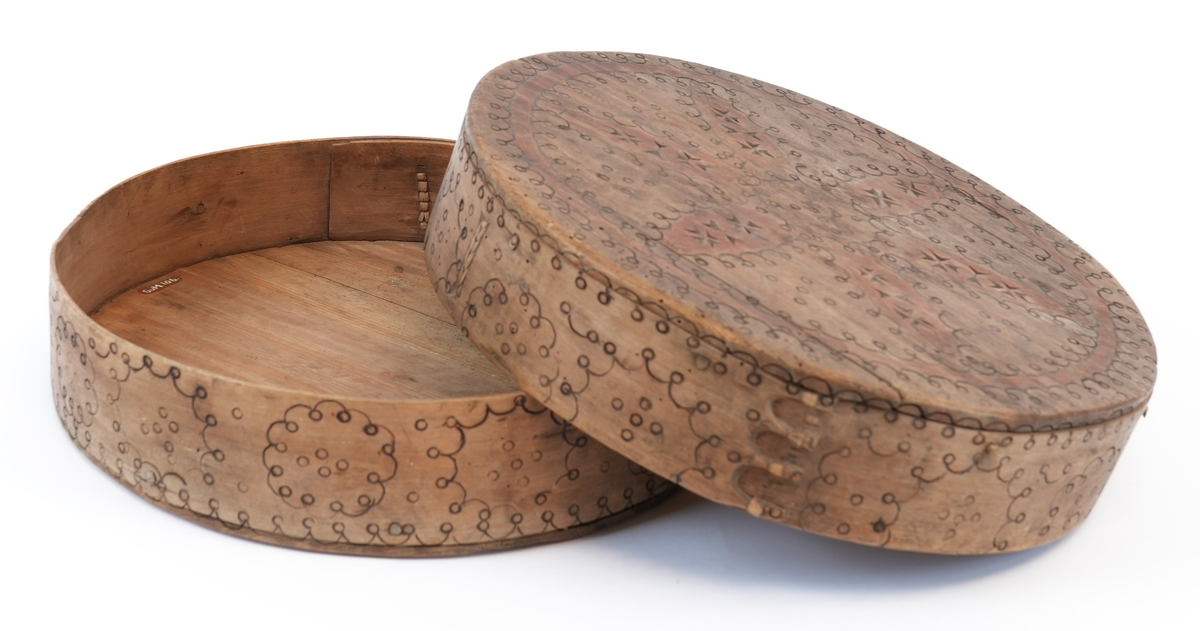 Svidekor over heile øskja. På toppen av lokket ei stor, sentral seksbladrose innskriven i ein sirkel med to melteserkors på kvert roseblad. Rosa og sirkelen måla raud. Langs sida sirklar av bogar og ringar. Alle linjene i ornamentet har form av svidde, små bogar og ringar.