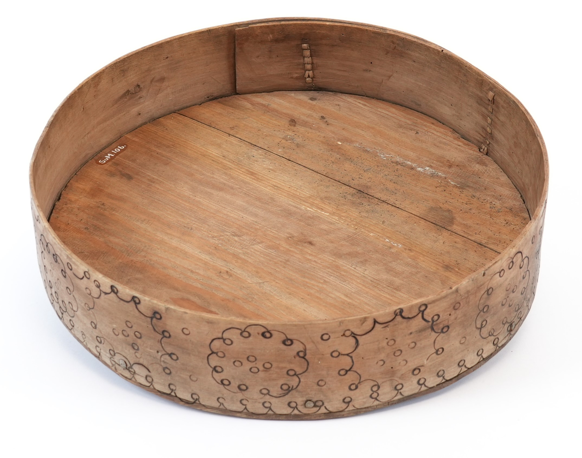 Svidekor over heile øskja. På toppen av lokket ei stor, sentral seksbladrose innskriven i ein sirkel med to melteserkors på kvert roseblad. Rosa og sirkelen måla raud. Langs sida sirklar av bogar og ringar. Alle linjene i ornamentet har form av svidde, små bogar og ringar.